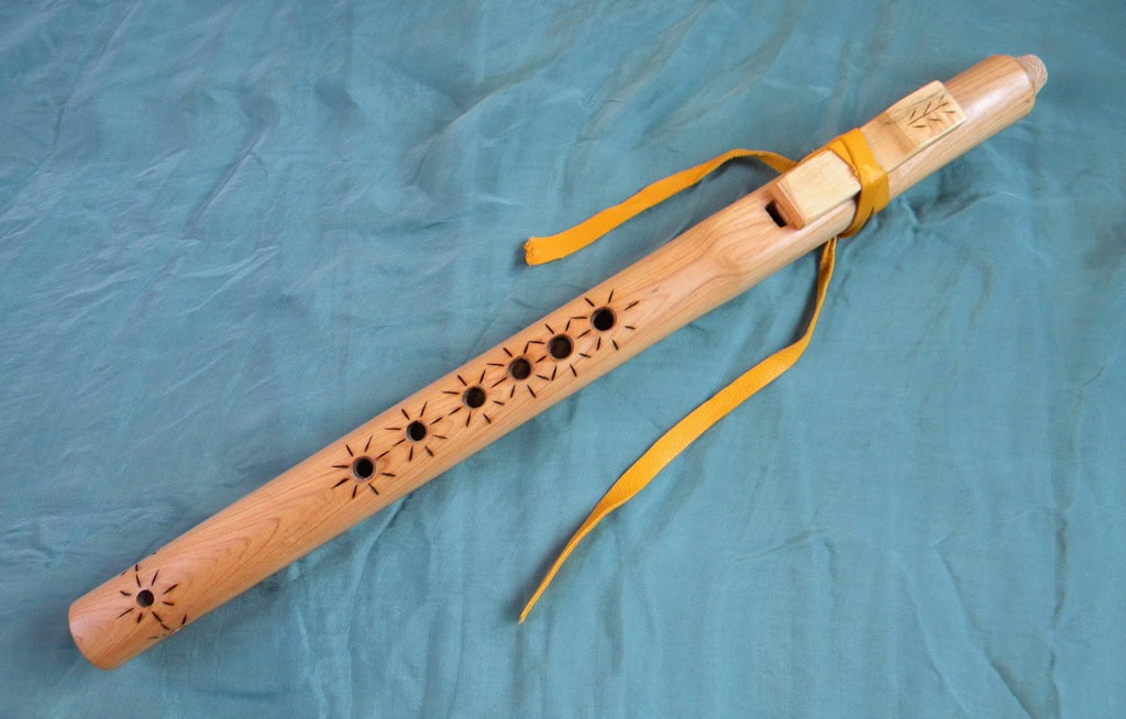 Native American style flute made of smooth, pale wood with 7 finger holes on the front.